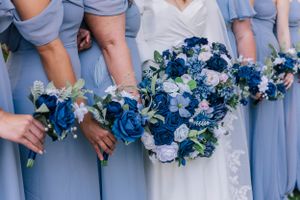 Bridesmaids in light blue dresses holding vibrant blue and white floral bouquets.