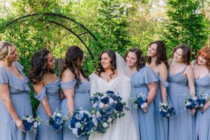 Wedding party group shot with bridesmaids in blue dresses holding bouquets outdoors.