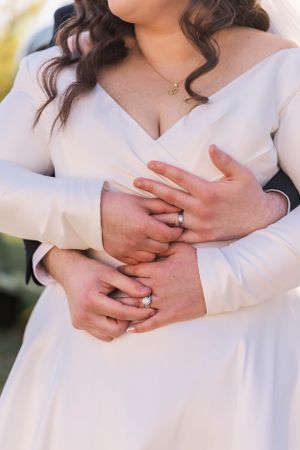 Close-up of hands with wedding rings against a white dress.