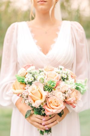 A bride in a white dress with puff sleeves holds a peach and cream rose bouquet.