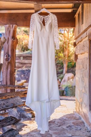 Elegant white lace wedding dress with long sleeves hanging in rustic wooden cabin setting.