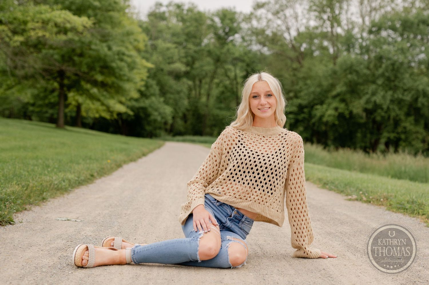 A casual outdoor portrait on a dirt path featuring a tan crochet sweater and distressed jeans.