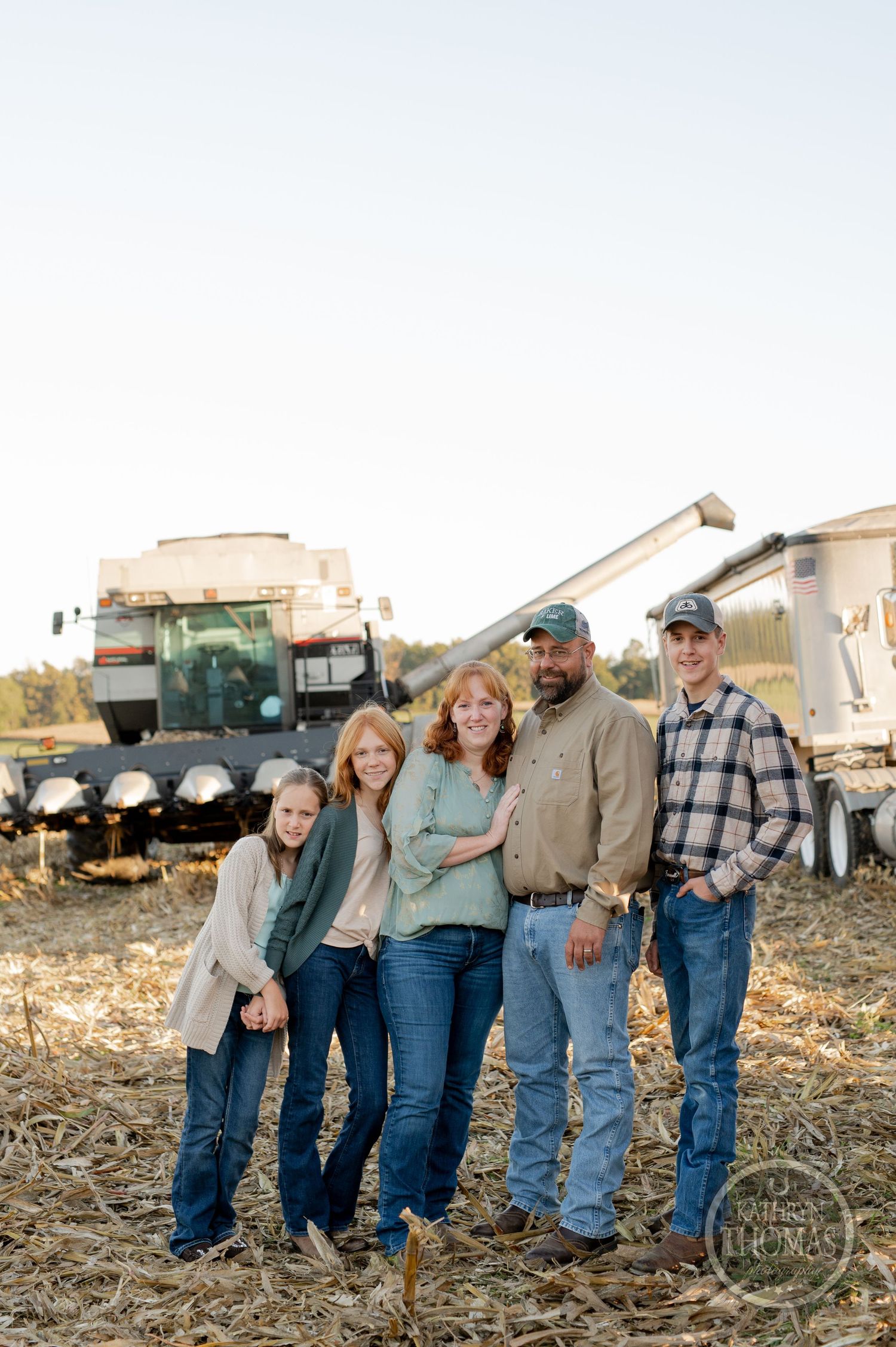 A family group stands together among farm equipment during golden hour.