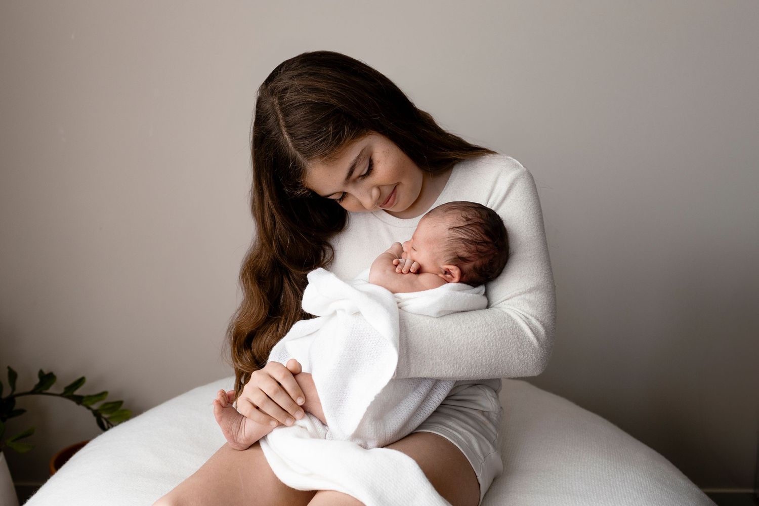 Tender moment in white as sister and newborn baby share an intimate bonding moment on a bed.
