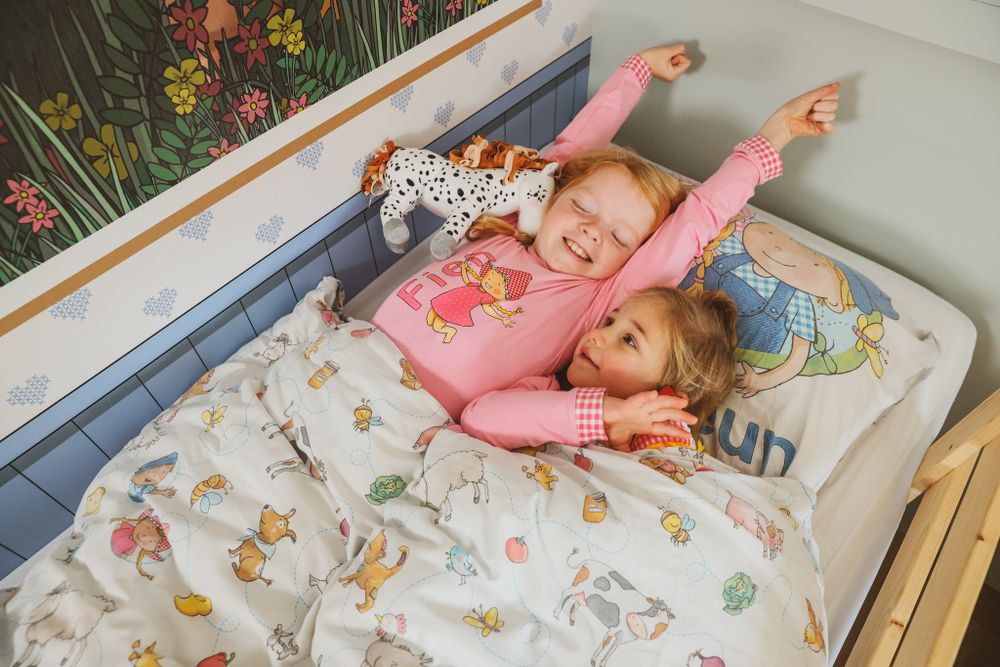 Two children in matching pajamas playing on bed with animal print bedding.
