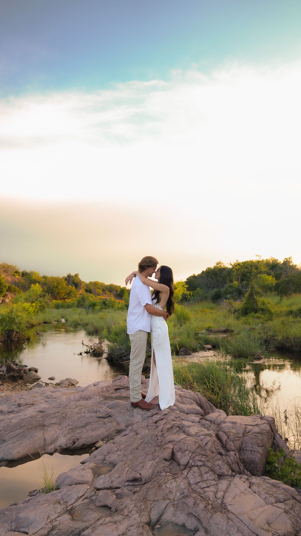 A floral dress is worn in a golden-hour photoshoot by a lake with warm sunlight filtering through trees.