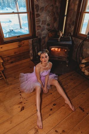 Ballerina in pink tutu posed near rustic wood stove with snowy window view.