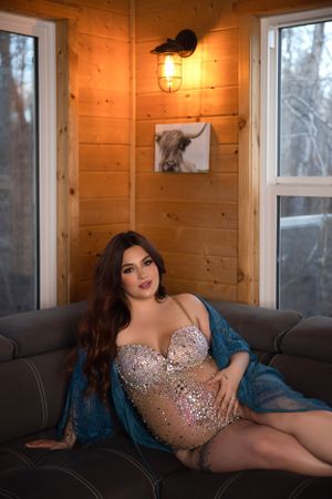An elegant maternity photo in a sequined dress with warm cabin lighting.