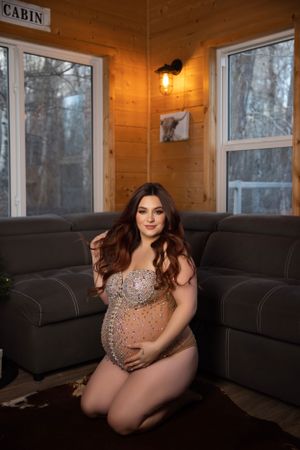 A maternity portrait in a sparkly dress inside a cozy wooden cabin.