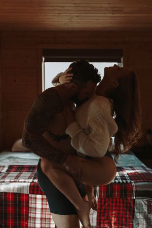 Romantic couple sharing intimate moment on plaid blanket in cabin setting.