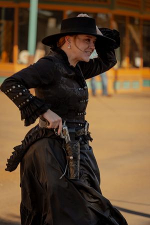 A dramatic fashion portrait featuring a black wide-brimmed hat and dark clothing against a warm-toned background.