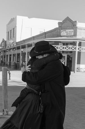Black and white panoramic view of a historic western town street with storefronts and wooden sidewalks.
