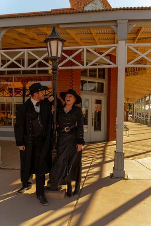 A series of silhouettes cast long shadows on a covered porch with white columns in an old western style setting.