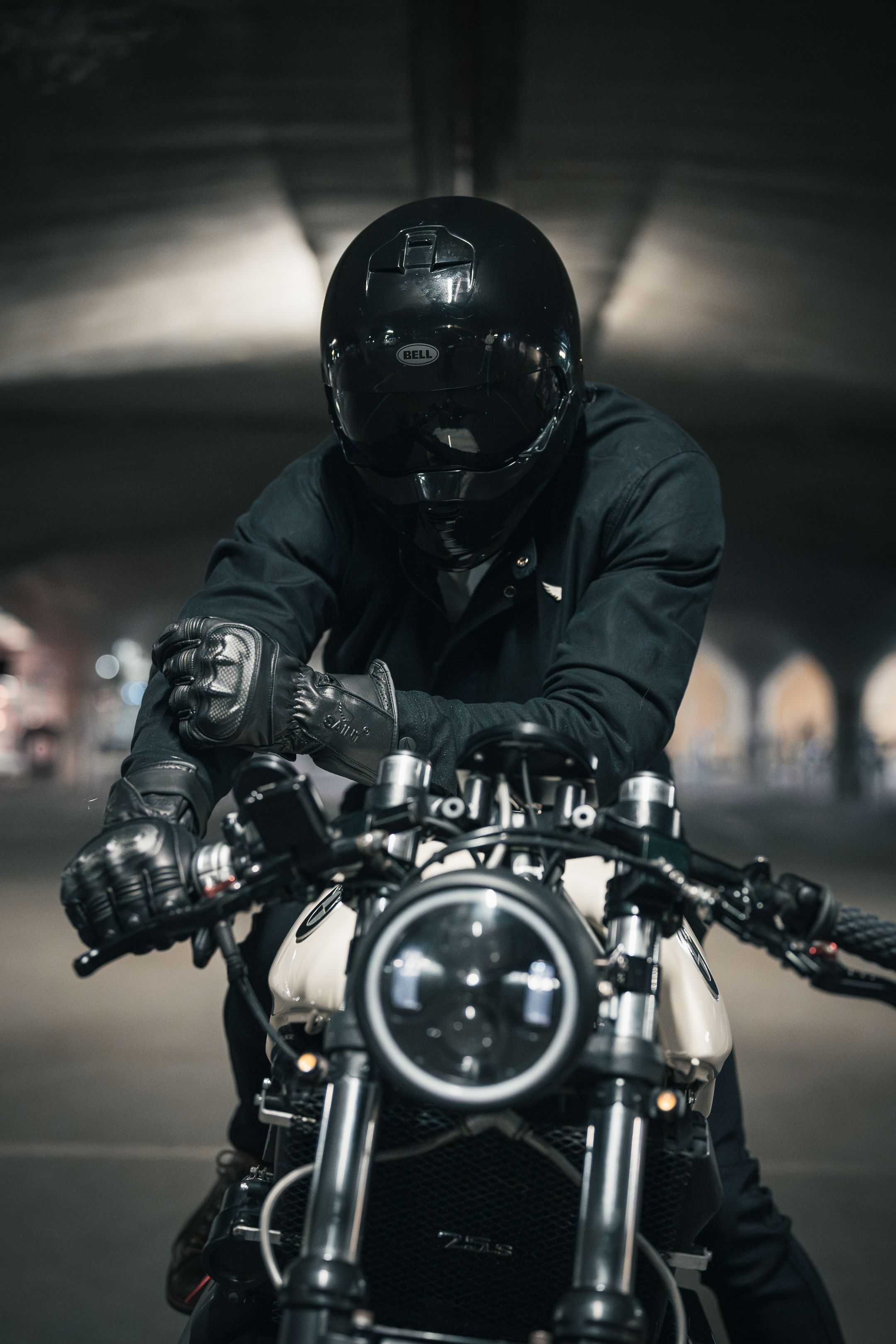 Rider in black helmet and gear on vintage-style motorcycle in moody lighting.