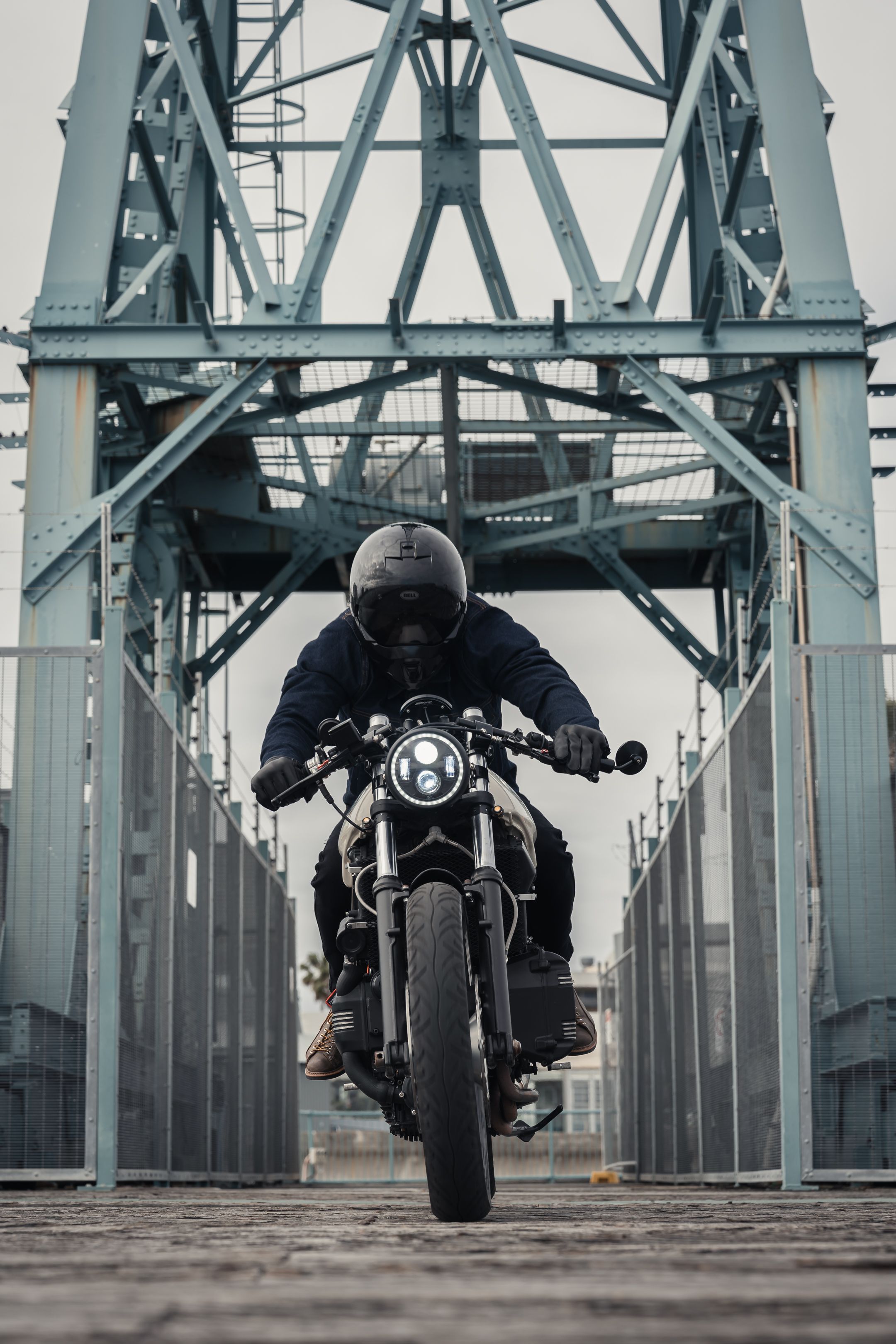 Motorcycle rider crossing steel bridge structure on vintage bike.