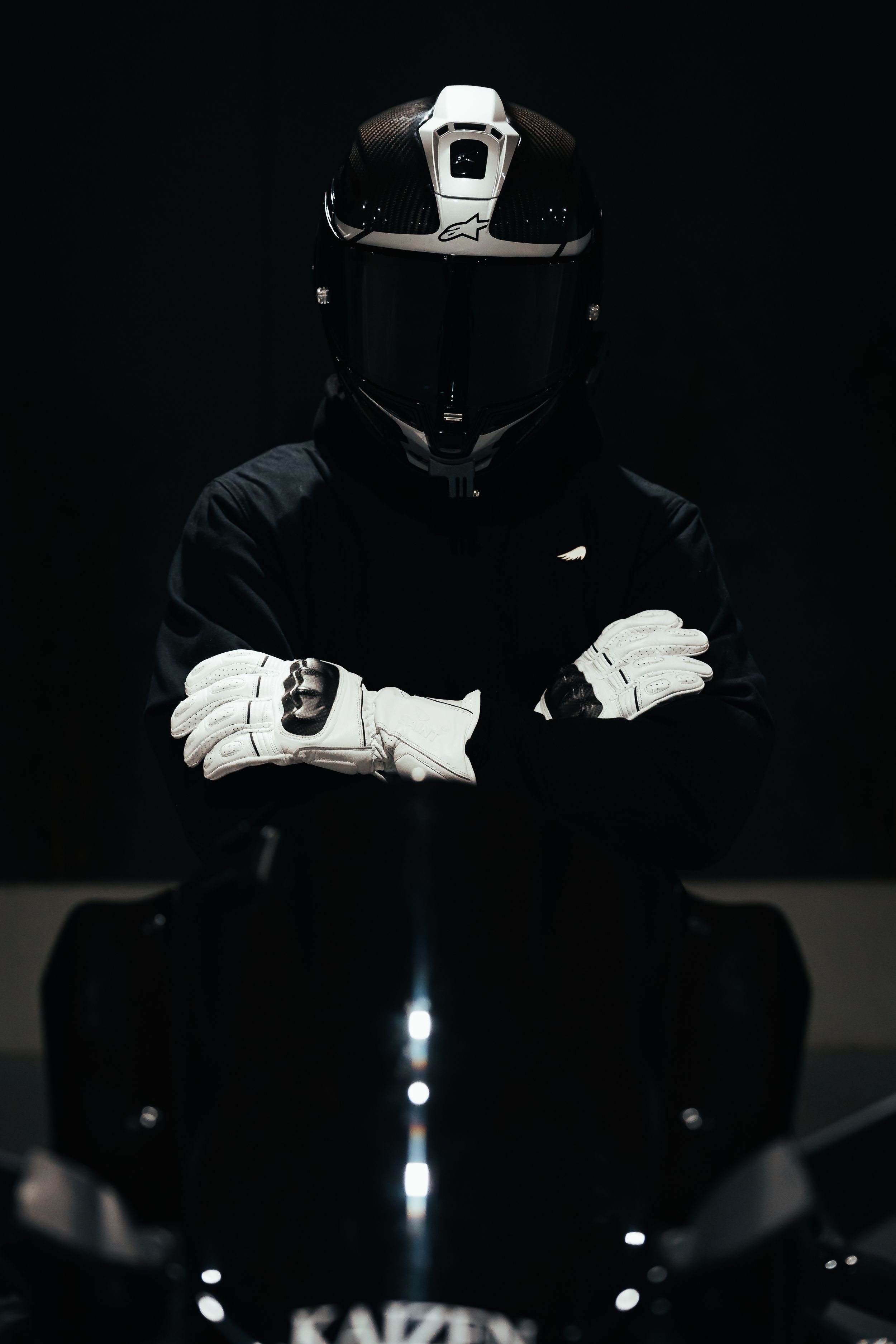 Dramatic low-key portrait of motorcyclist in black gear and white helmet against dark background.