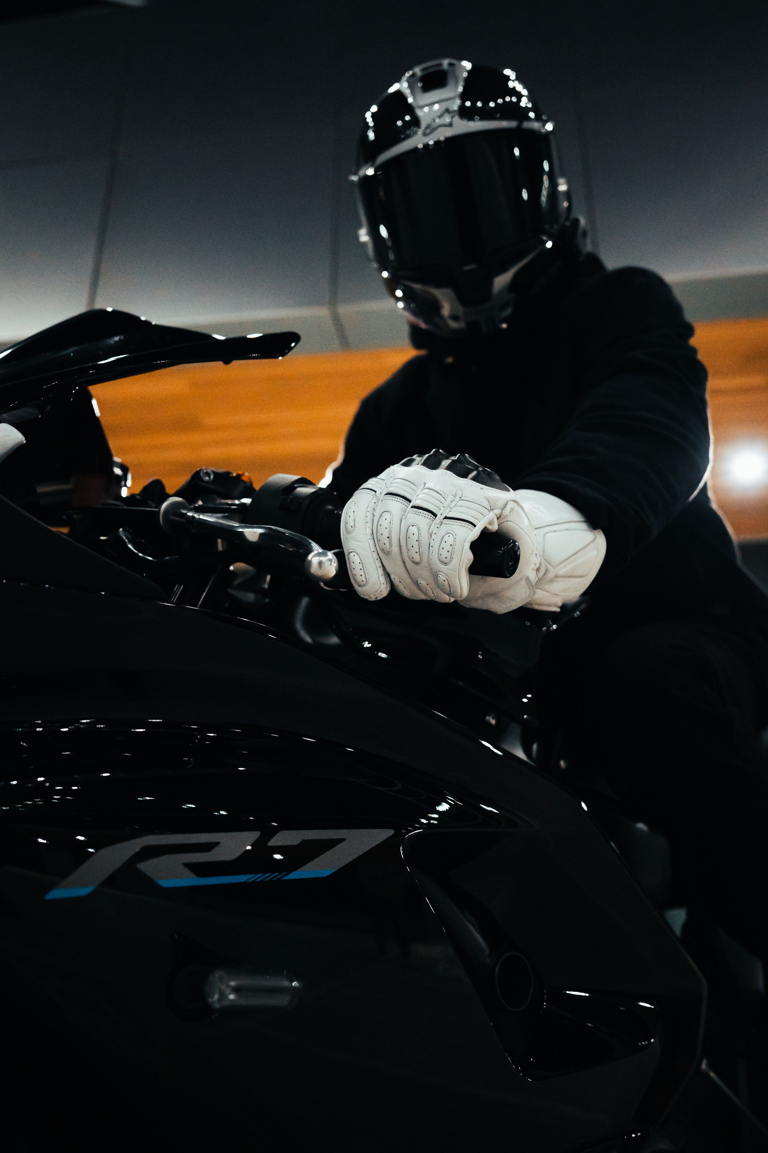 Close-up of motorcyclist in black gear and white gloves gripping handlebars.