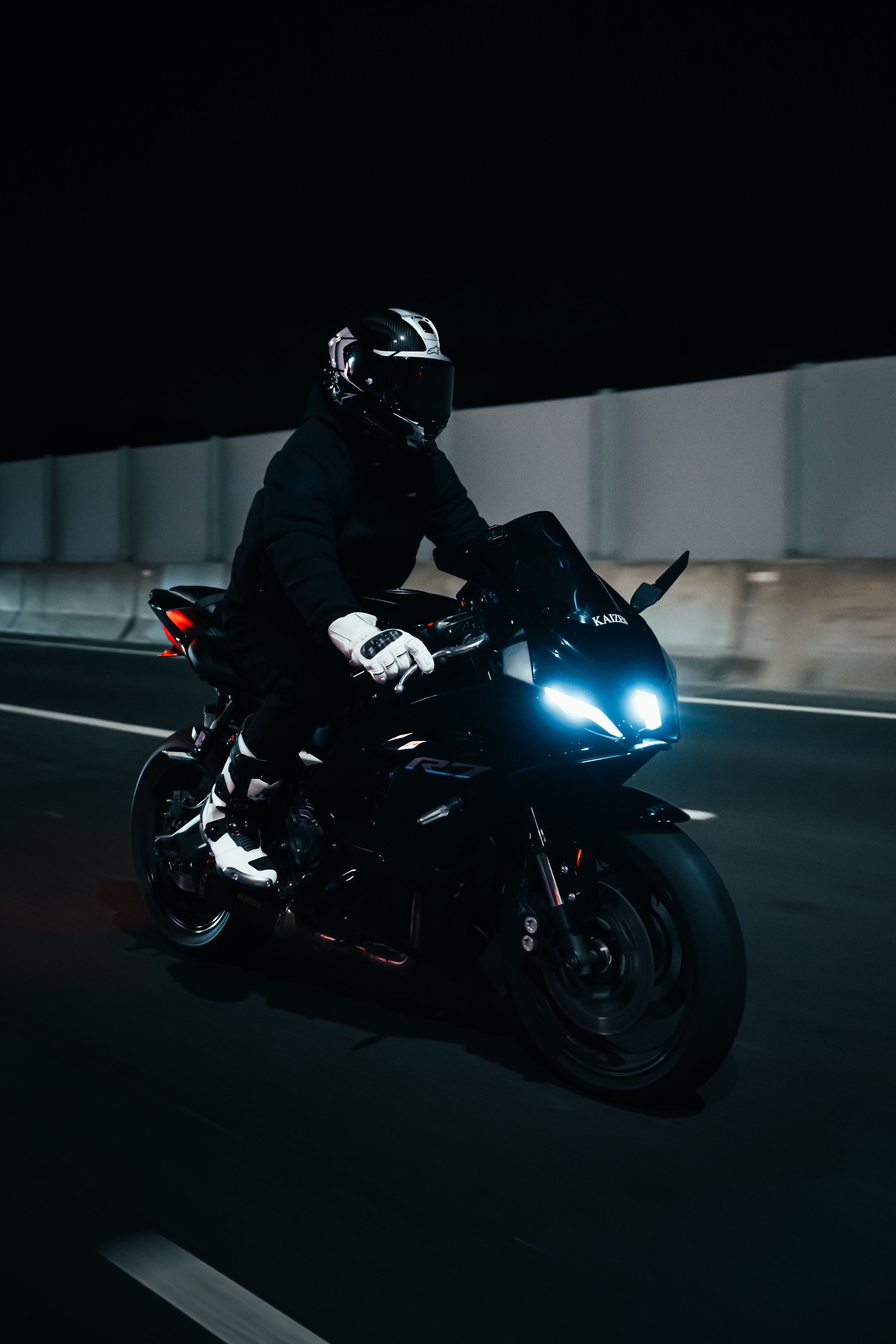 Motorcyclist in black gear riding sports bike with glowing blue headlights at night.