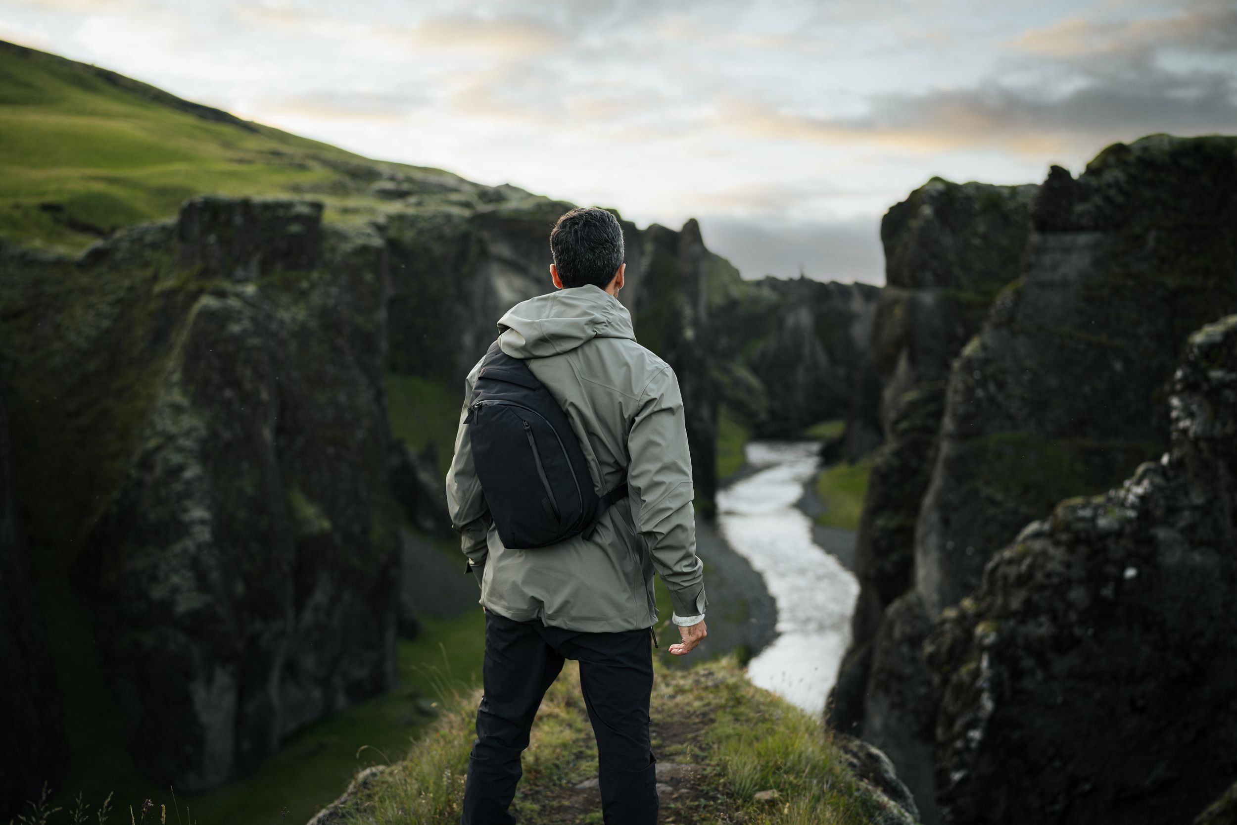 Hiker overlooking dramatic canyon with winding river below in moody landscape.