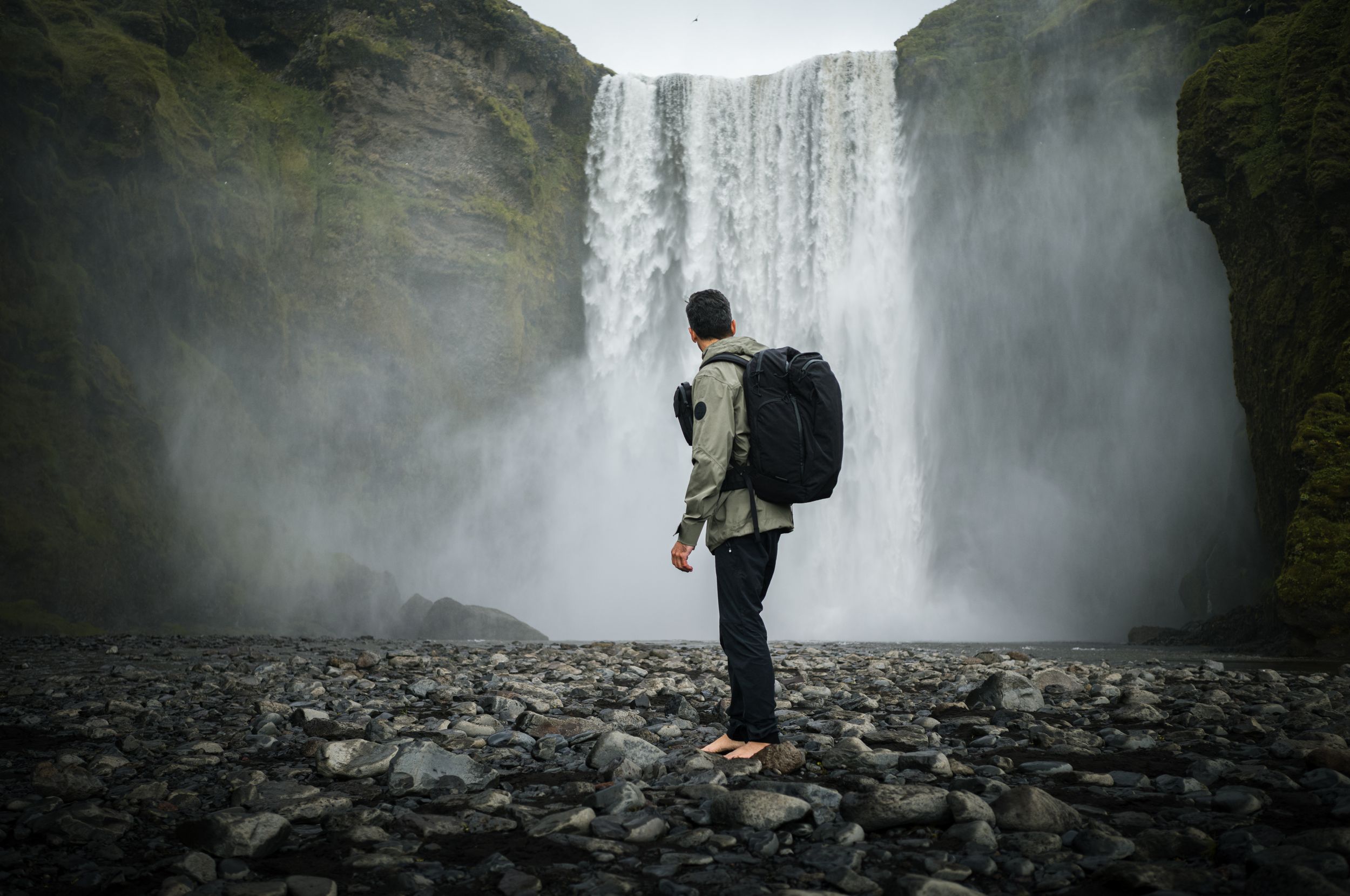 Solo traveler admiring massive waterfall while standing on rocky shore.