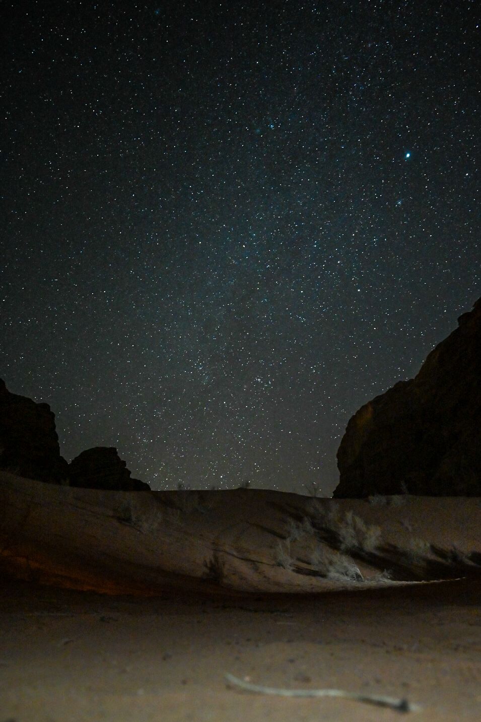 Starry night sky framed by silhouetted desert rock formations.