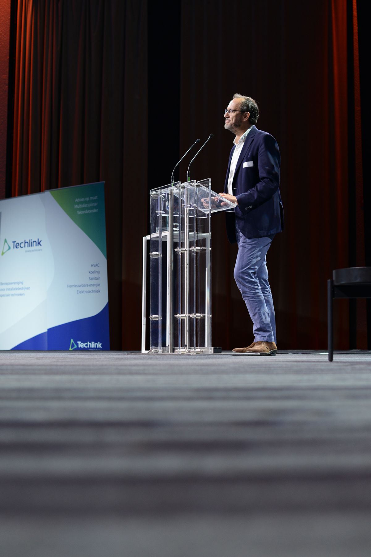 Speaker presenting at a professional conference with transparent podium on stage.