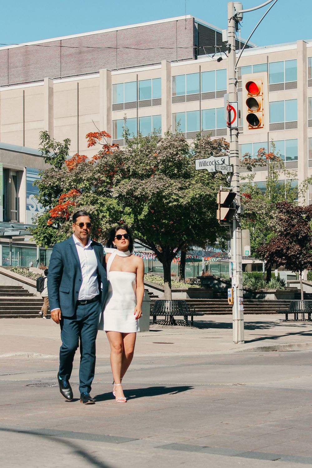 Stylish couple walking together on an urban sidewalk with modern building and traffic lights.