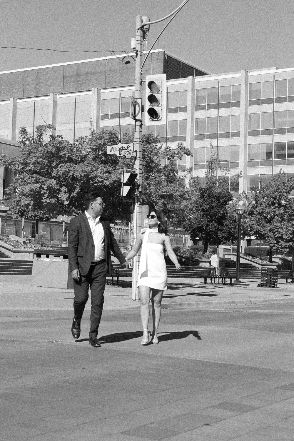A black and white photo of a couple walking together on an urban sidewalk.