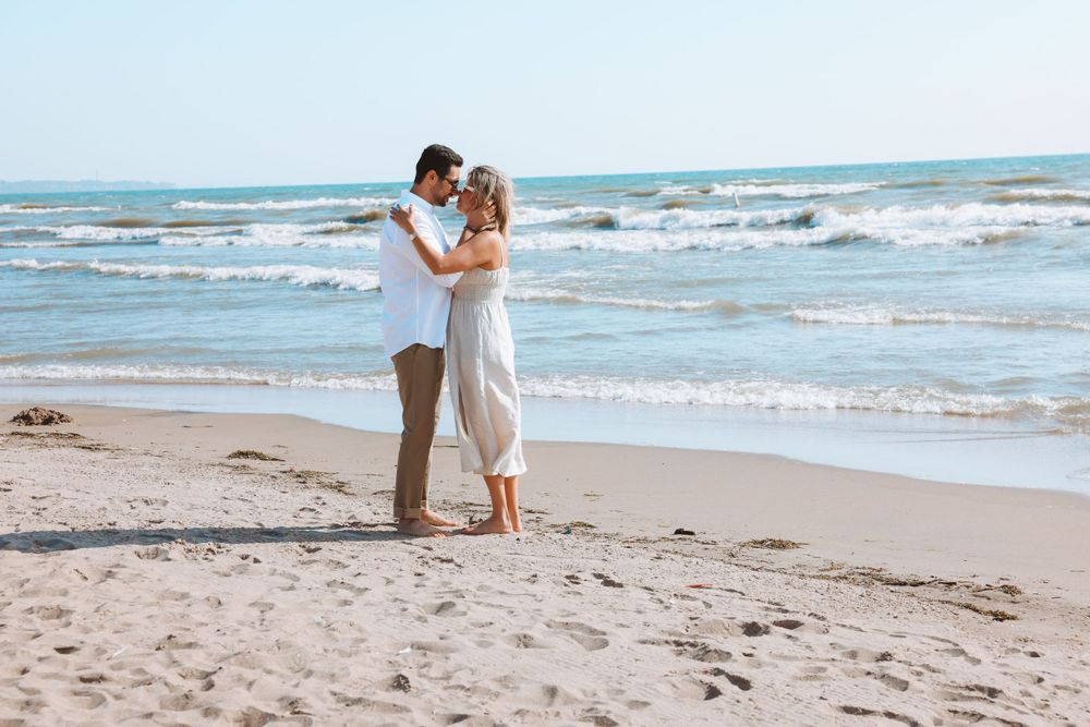 A romantic couple shares an embrace on a sandy beach with waves rolling in.