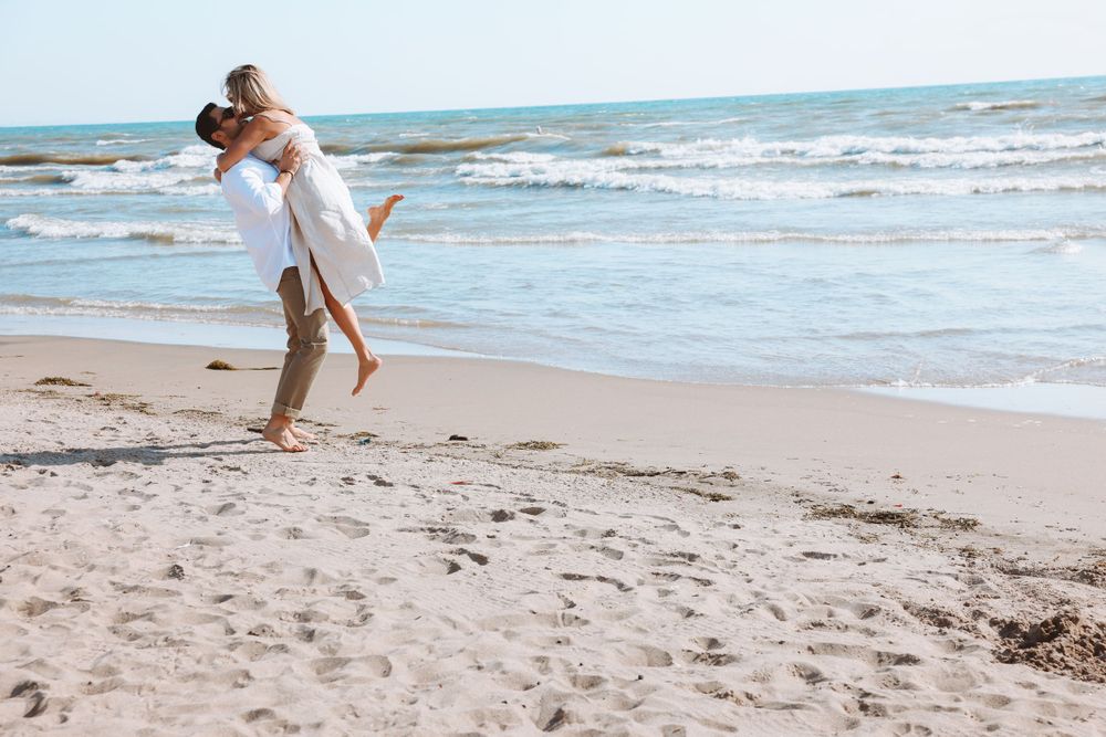 A playful couple shares a romantic moment while standing on a sandy beach.