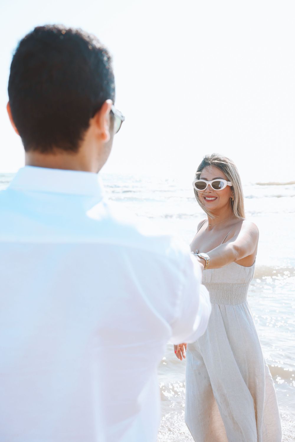 A couple enjoys a romantic moment on a sunny beach with the ocean waves in the background.