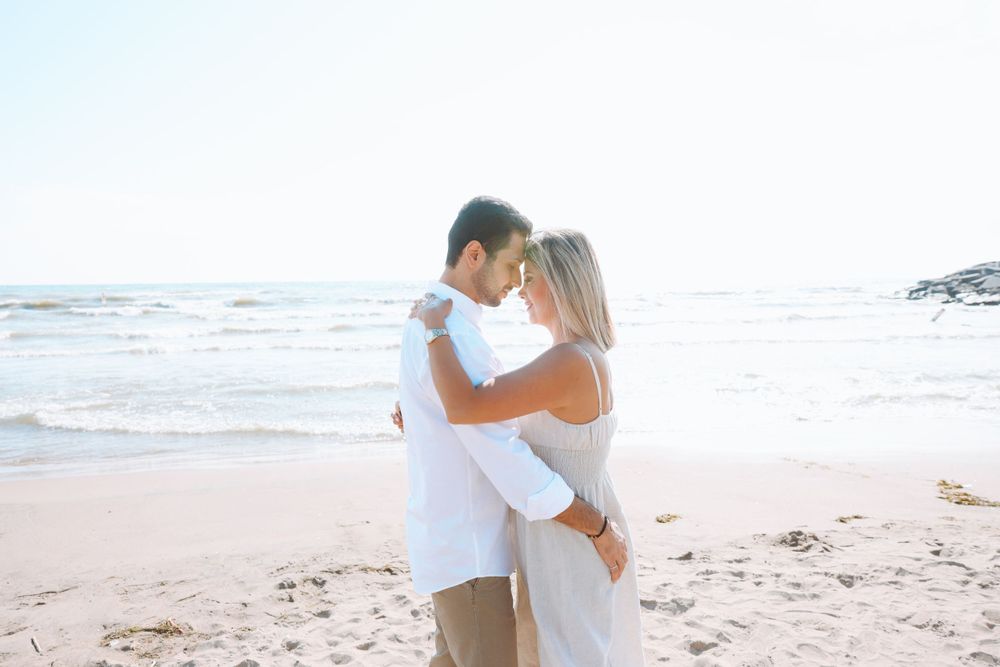 A tender beach embrace between two people dressed in white against an ocean backdrop.