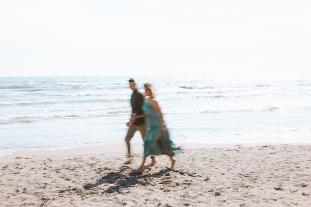 A playful couple runs together along the shoreline at the beach.