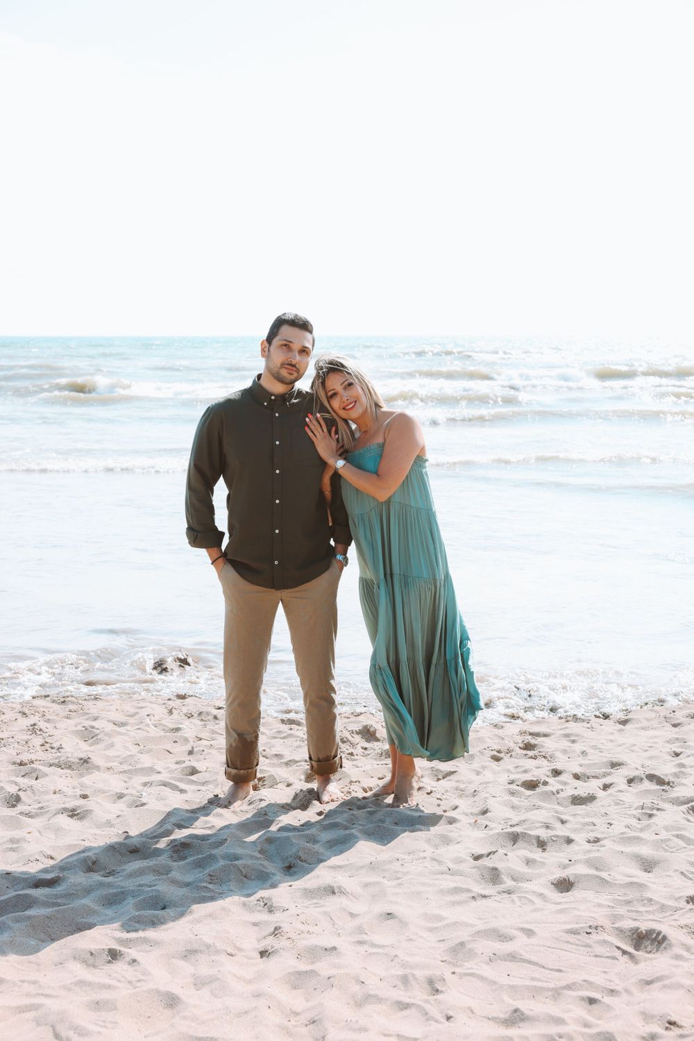 A couple poses together on a sunny beach wearing coordinated casual outfits.