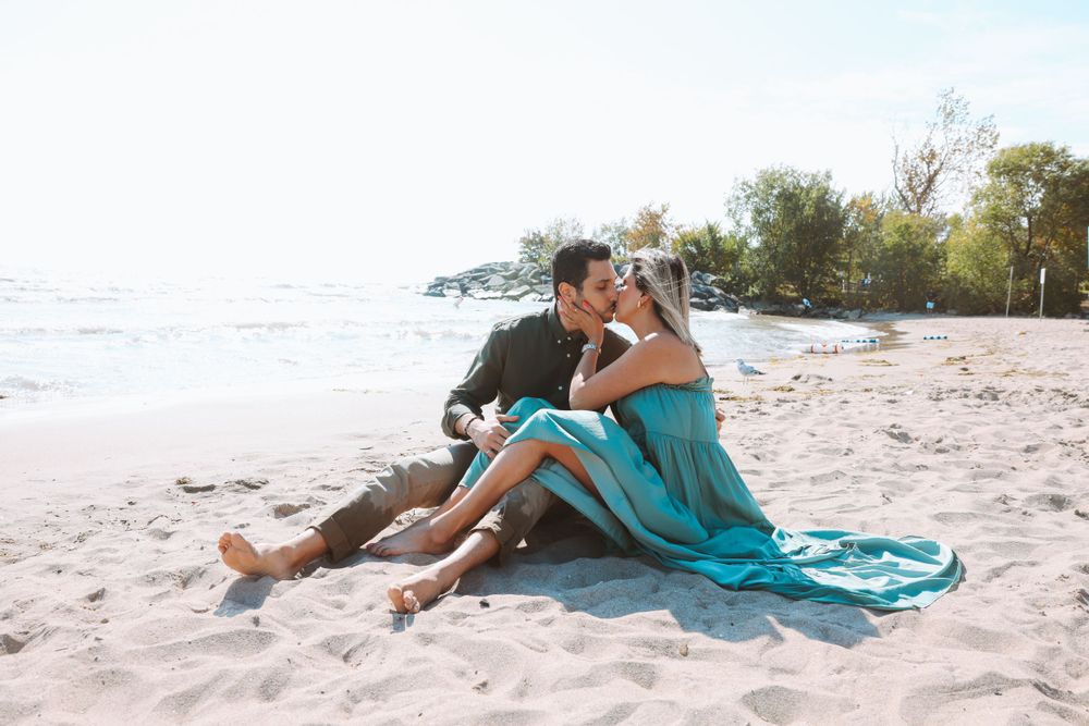 Romantic beach photoshoot with couple sitting on sand in teal dress and casual wear.