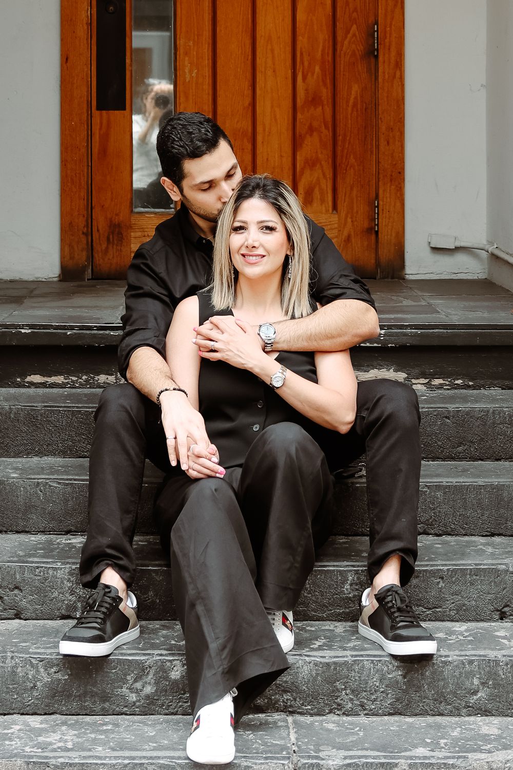 A couple in matching black outfits sharing an intimate moment on stone steps.