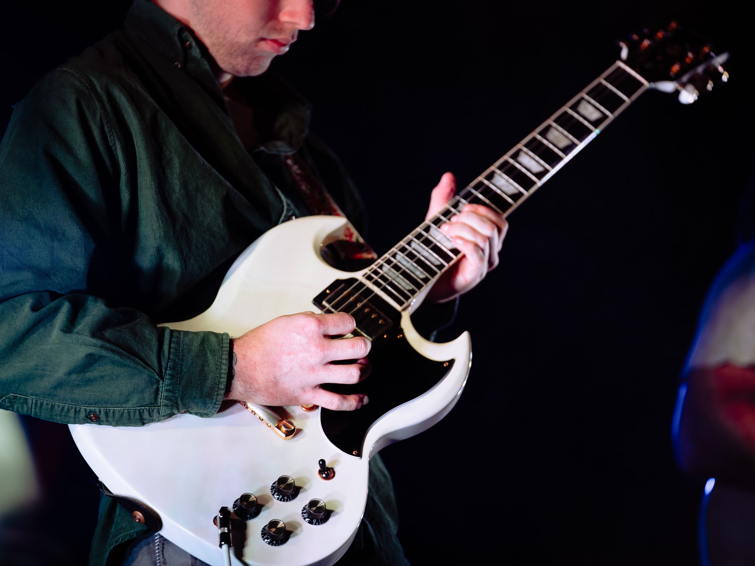 Close-up shot of hands playing white electric guitar during performance.