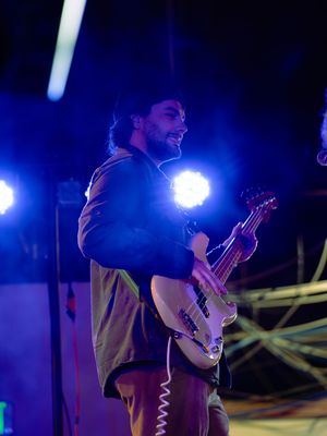 Musicians perform on a dark stage illuminated by bright blue spotlights during a nighttime concert.