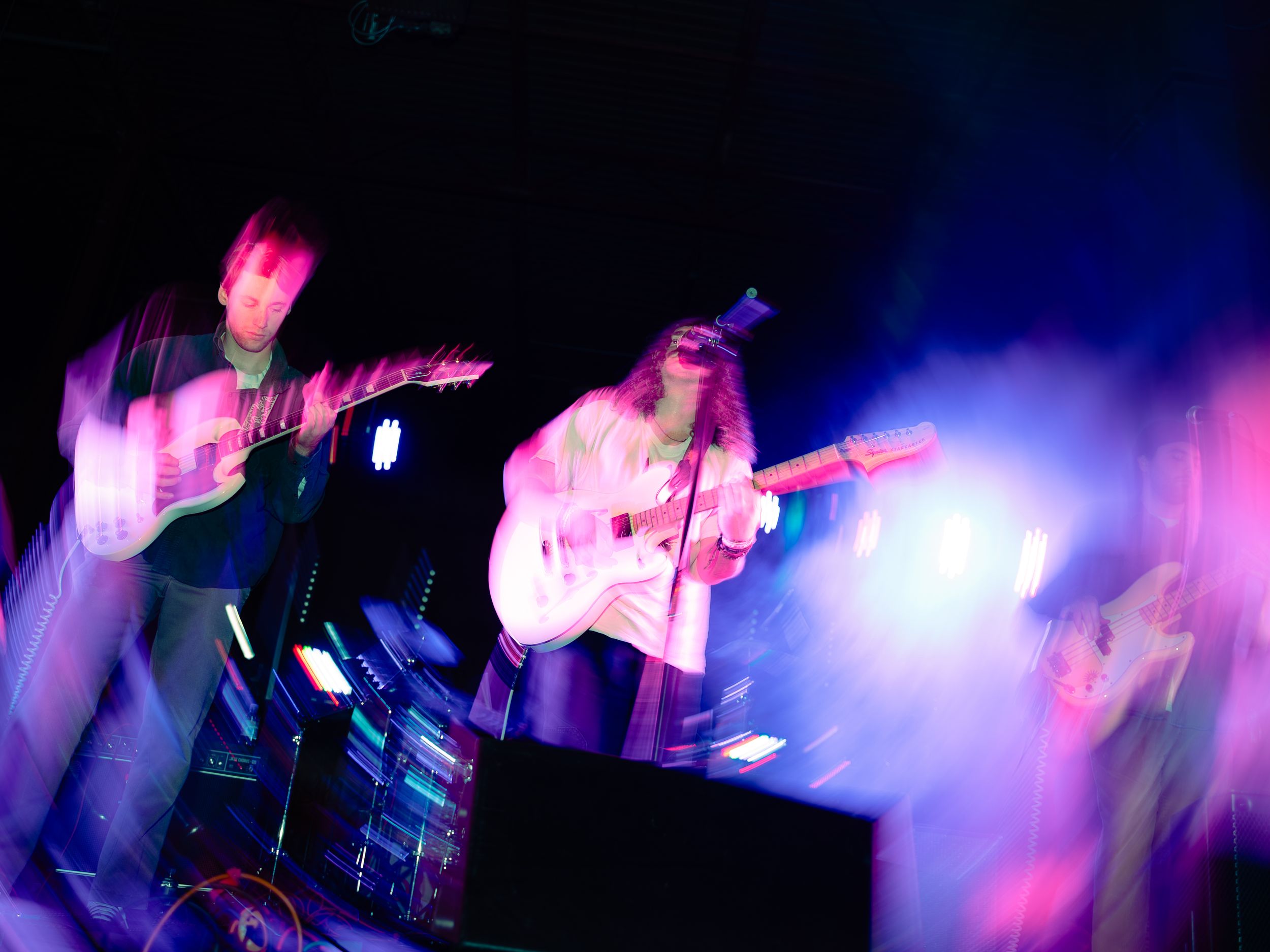 Concert scene with musicians performing on stage bathed in purple and blue lighting effects.