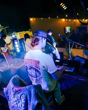 Musicians performing on stage with blue lighting and concert equipment visible in the background.