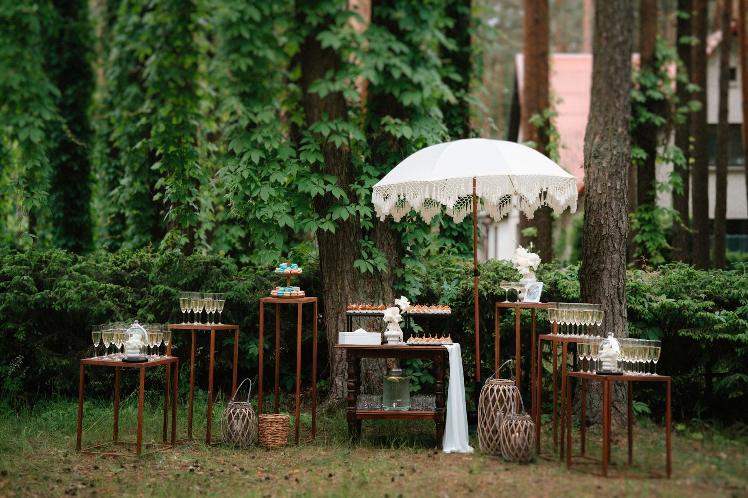 Outdoor wedding reception setup in a pine forest with white tables and decor.