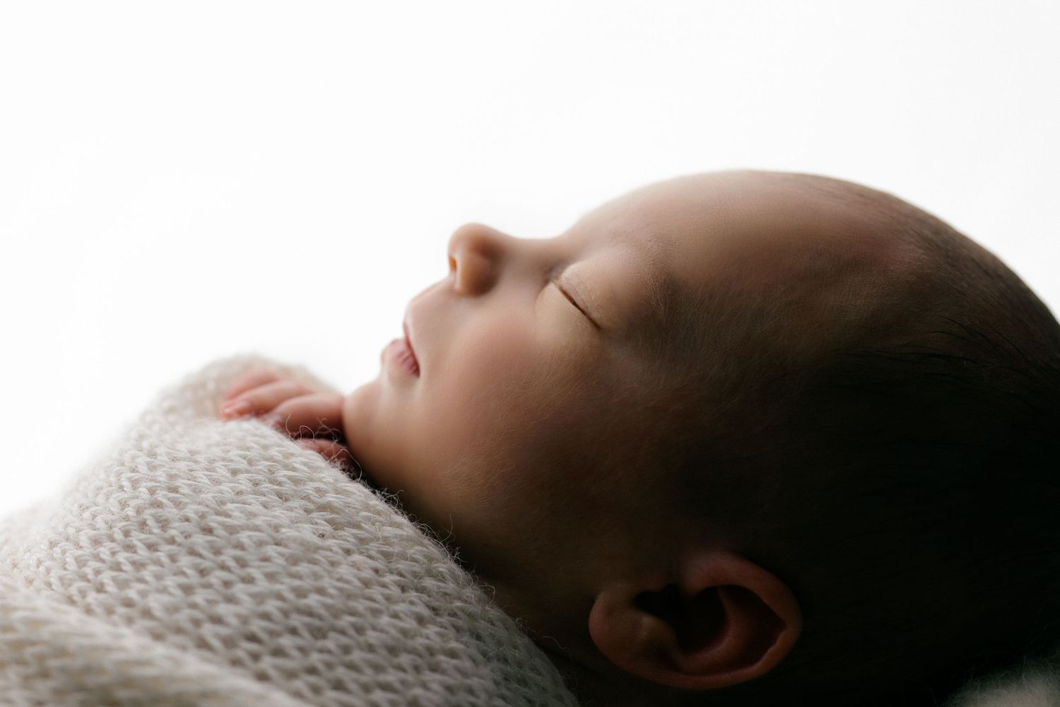 Peaceful newborn baby sleeping wrapped in a soft knit blanket, eyes closed in serene slumber.