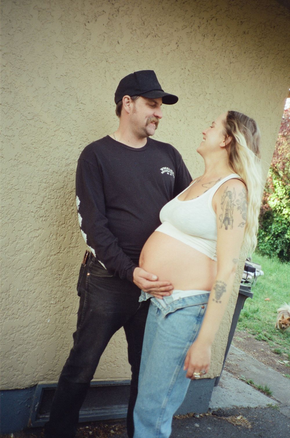 Couple sharing a tender moment outdoors, man touching pregnant womans baby bump against yellow wall.