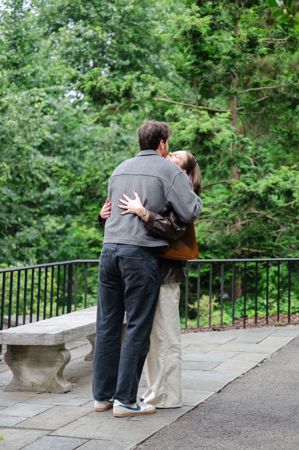 Couple embracing on a stone terrace surrounded by lush green trees in a garden setting.