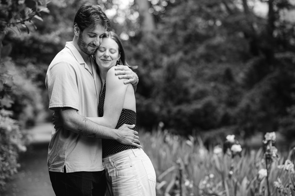 Black and white photo of a couple embracing tenderly in a lush garden, the woman leaning into the man's arms.
