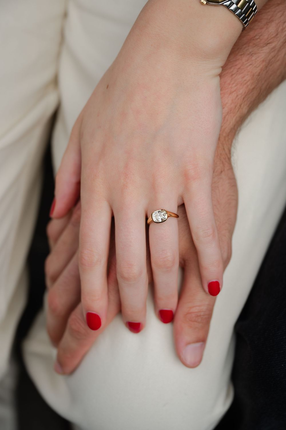 Close-up of engagement ring with large diamond on womans hand with red nails resting on mans hand.