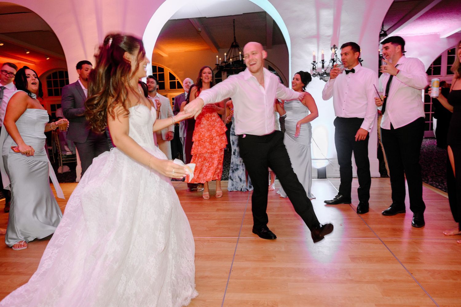 Bride and groom dancing joyfully at wedding reception surrounded by guests in elegant venue.