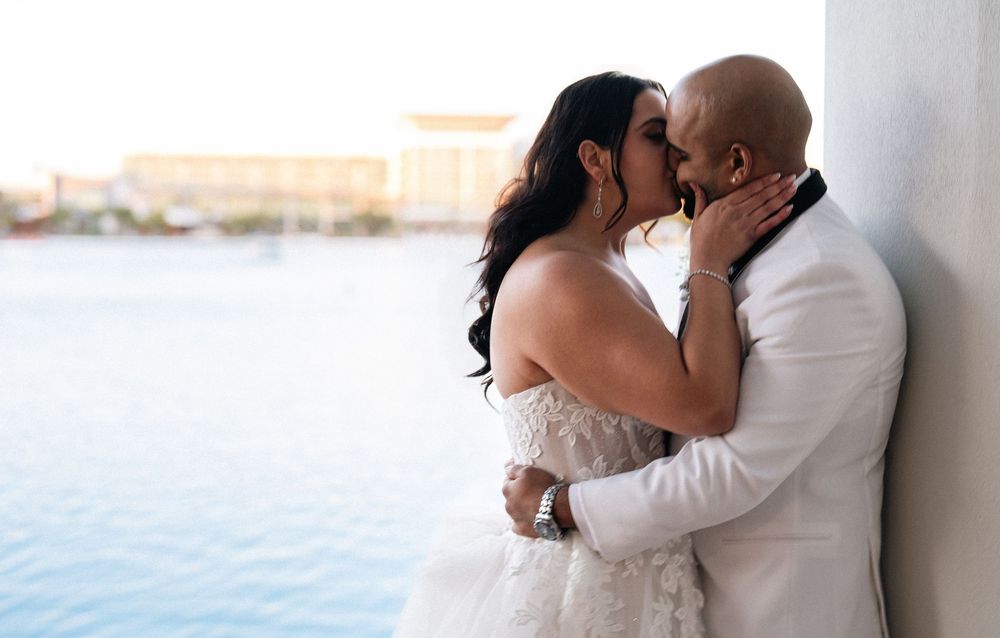 A bride and groom share a romantic kiss outdoors near a waterfront on their wedding day.