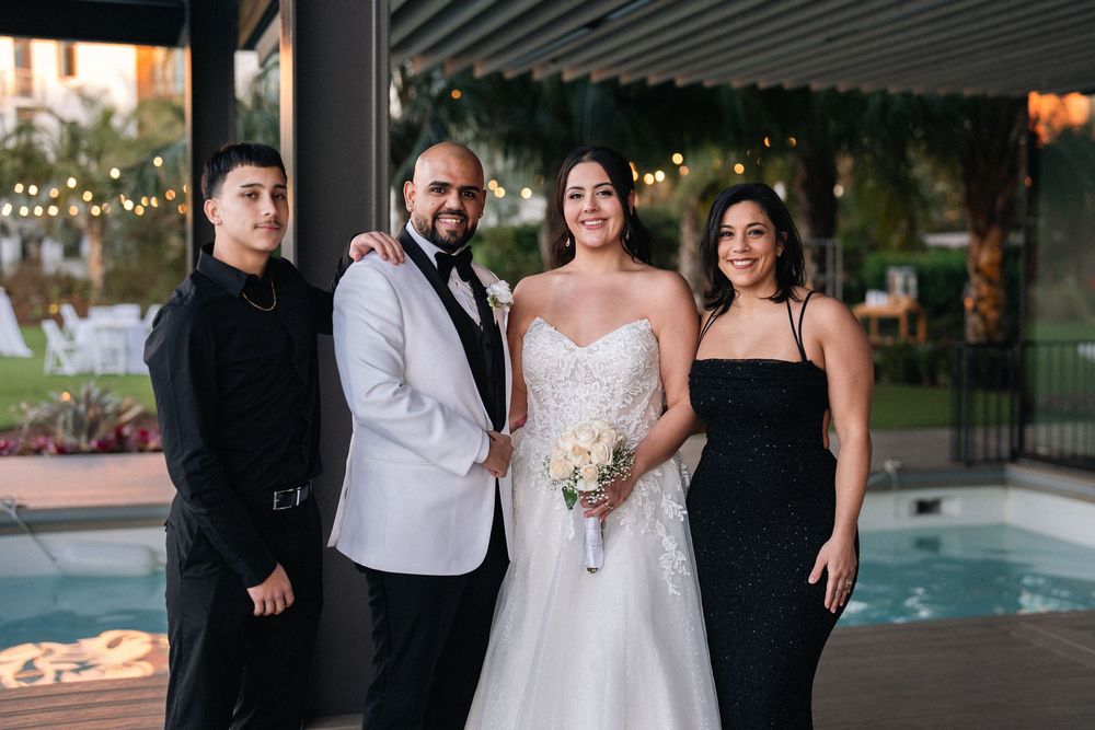 Bride and groom pose with two guests poolside at an elegant outdoor wedding reception.