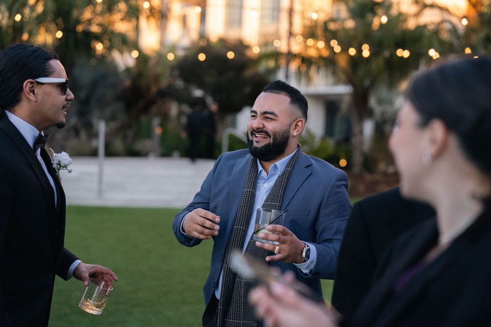 Two men in suits laughing and holding drinks at an outdoor evening cocktail reception.